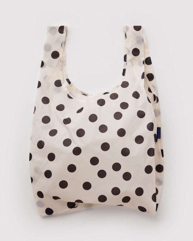 A reusable plastic shopping bag with a cream background and dark brown polka dots, shown against a light gray background.