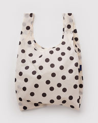 A reusable plastic shopping bag with a cream background and dark brown polka dots, shown against a light gray background.