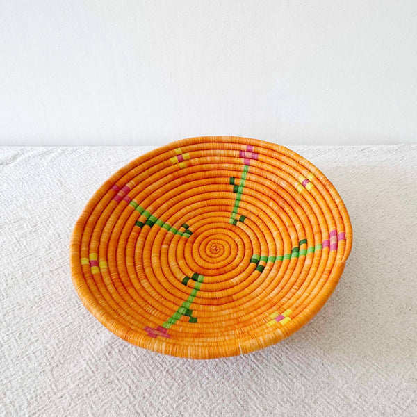 Woven orange basket with colorful patterns on a white surface