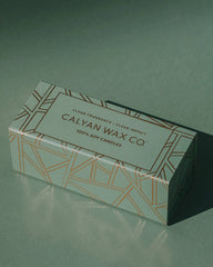 A box of Calyan Wax Co. soy candles on a dark green surface with a soft shadow.