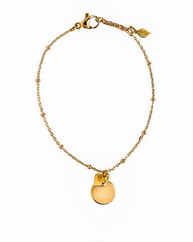 A delicate gold chain bracelet with a small round disc charm engraved with love displayed on a clean white background.