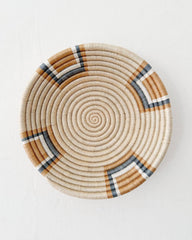 A round woven basket plate with a spiral pattern in natural beige, brown, and dark gray, photographed from directly above on a white background.