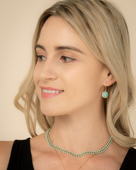 Woman wearing a green necklace and earrings against a beige background