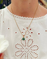 Person wearing a gold necklace with a green pendant on a white blouse.