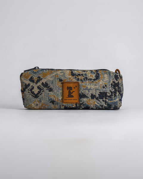 A rectangular zippered pouch with a woven geometric pattern in blue, gold, and gray, featuring a brown leather patch with a black silhouette logo and the text New Hope Girls 