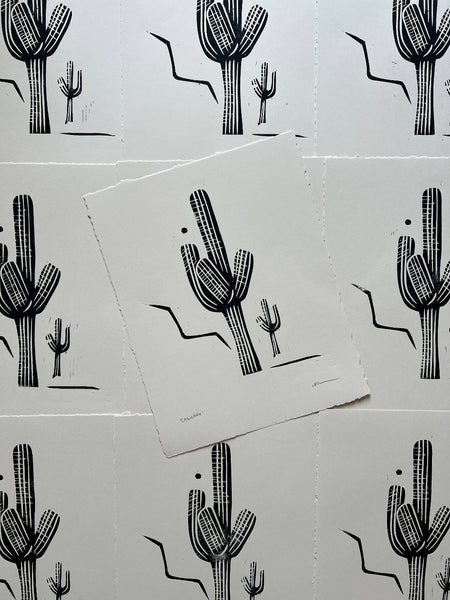 Black cactus illustrations on white paper with a pattern of additional cacti in the background.