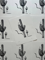Black cactus illustrations on white paper with a pattern of additional cacti in the background.