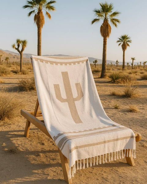 Beige blanket with cactus design draped over a wooden chair in a desert setting with palm trees.