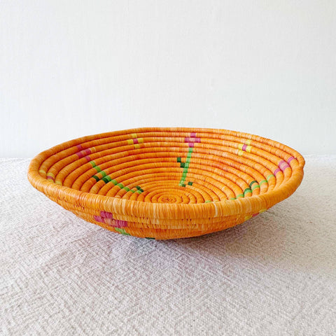 Woven orange basket with colorful patterns on a white surface
