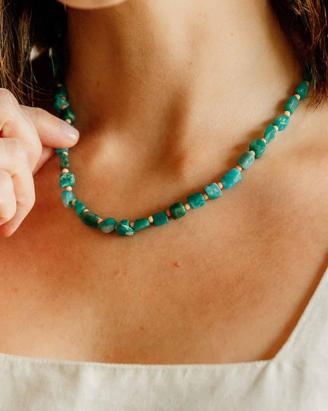 Person wearing a green beaded necklace with a neutral background