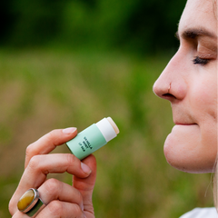 Person holding a green lip balm stick outdoors with a blurred natural background