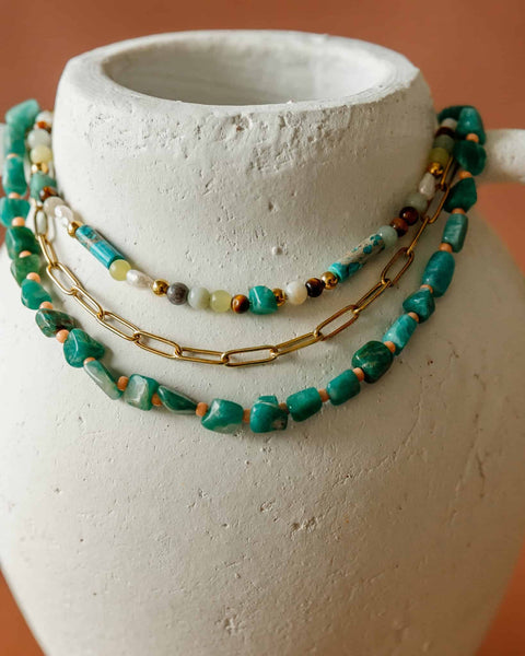 Necklace with green beads and gold chain on a white ceramic vase against an orange background