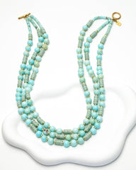 Multistrand beaded necklace with turquoise and green beads on a white stand.