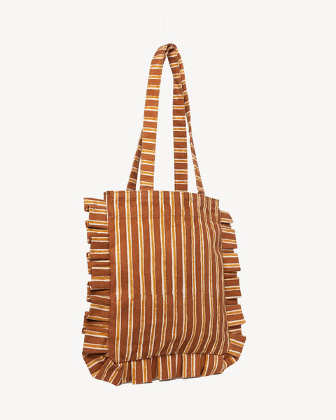 A vertical striped tote bag in brown and beige with fringed edges and matching shoulder straps, shown against a plain off-white background.