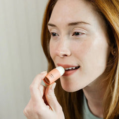 Woman applying lip balm with a neutral background