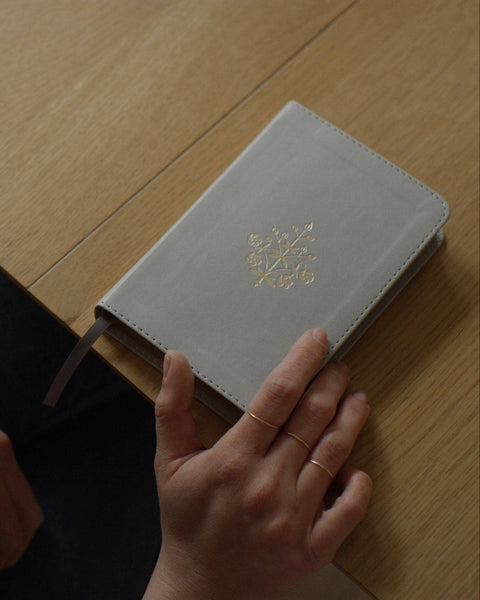 Gray notebook with a gold emblem on a wooden surface, held by a person.