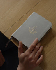 Gray notebook with a gold emblem on a wooden surface, held by a person.