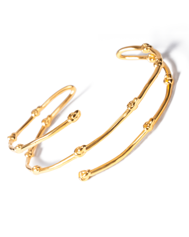 A gold-toned open cuff bracelet with a textured, branch-like segmented design, photographed on a clean white background with a soft shadow.