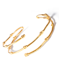 A gold-toned open cuff bracelet with a textured, branch-like segmented design, photographed on a clean white background with a soft shadow.