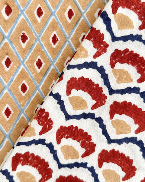 Two folded fabrics with distinct patterns shown side-by-side. The left fabric features a tan and light blue diamond lattice pattern with red diamond accents.