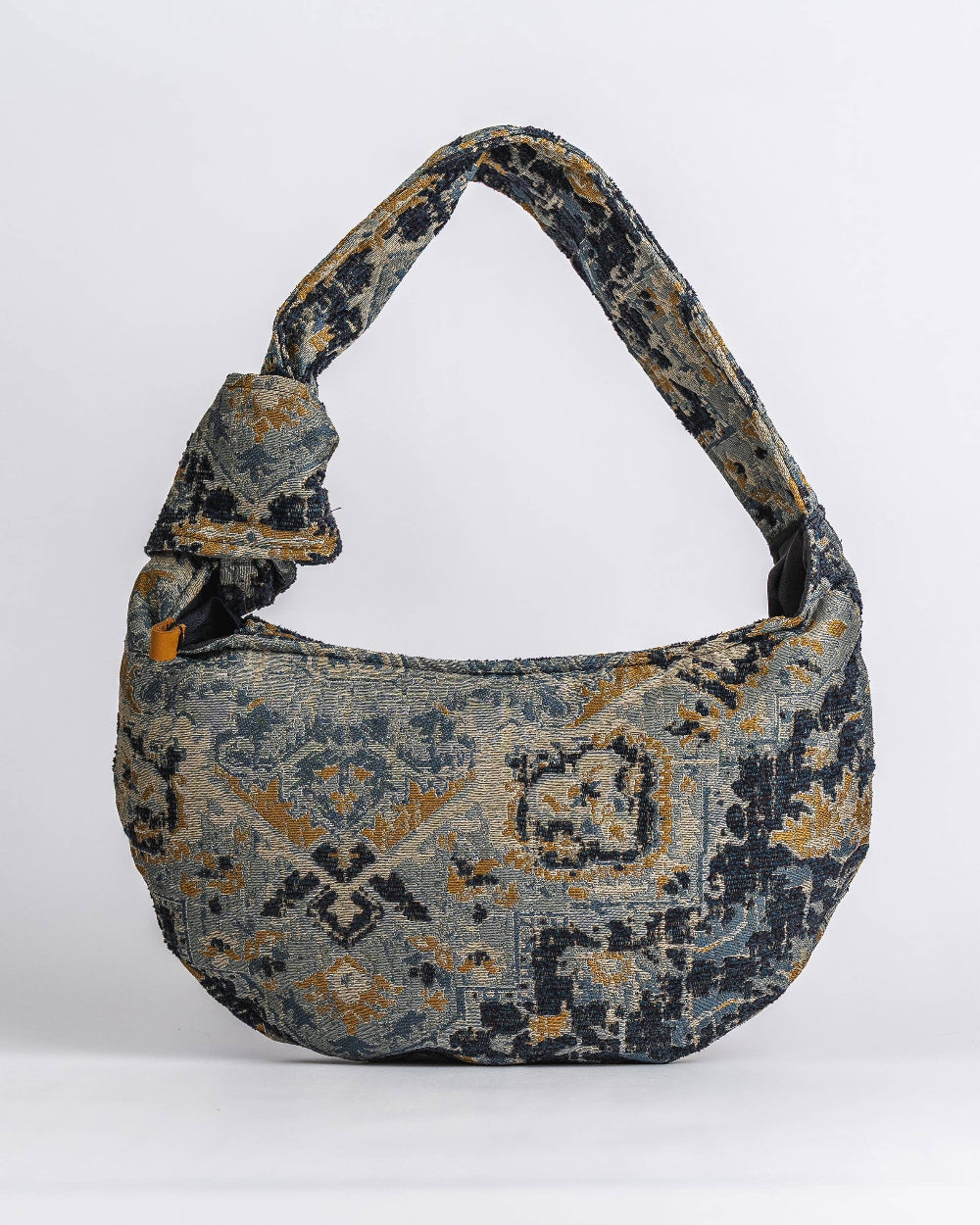 A slouchy shoulder bag with a distressed, vintage-style geometric pattern in navy blue, gray, and ochre yellow, set against a plain light gray background.