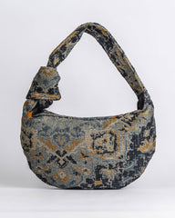 A slouchy shoulder bag with a distressed, vintage-style geometric pattern in navy blue, gray, and ochre yellow, set against a plain light gray background.