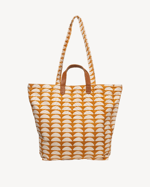 A canvas tote bag featuring a repeating orange and cream semicircle pattern, with brown leather top handles and a matching braided shoulder strap, shown against a plain off-white background.