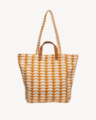 A canvas tote bag featuring a repeating orange and cream semicircle pattern, with brown leather top handles and a matching braided shoulder strap, shown against a plain off-white background.