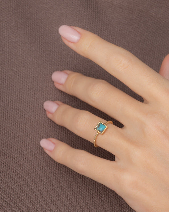 Hand wearing a gold ring with a turquoise stone on a brown background