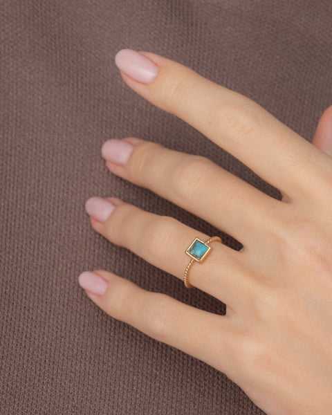 Hand wearing a gold ring with a turquoise stone on a brown background