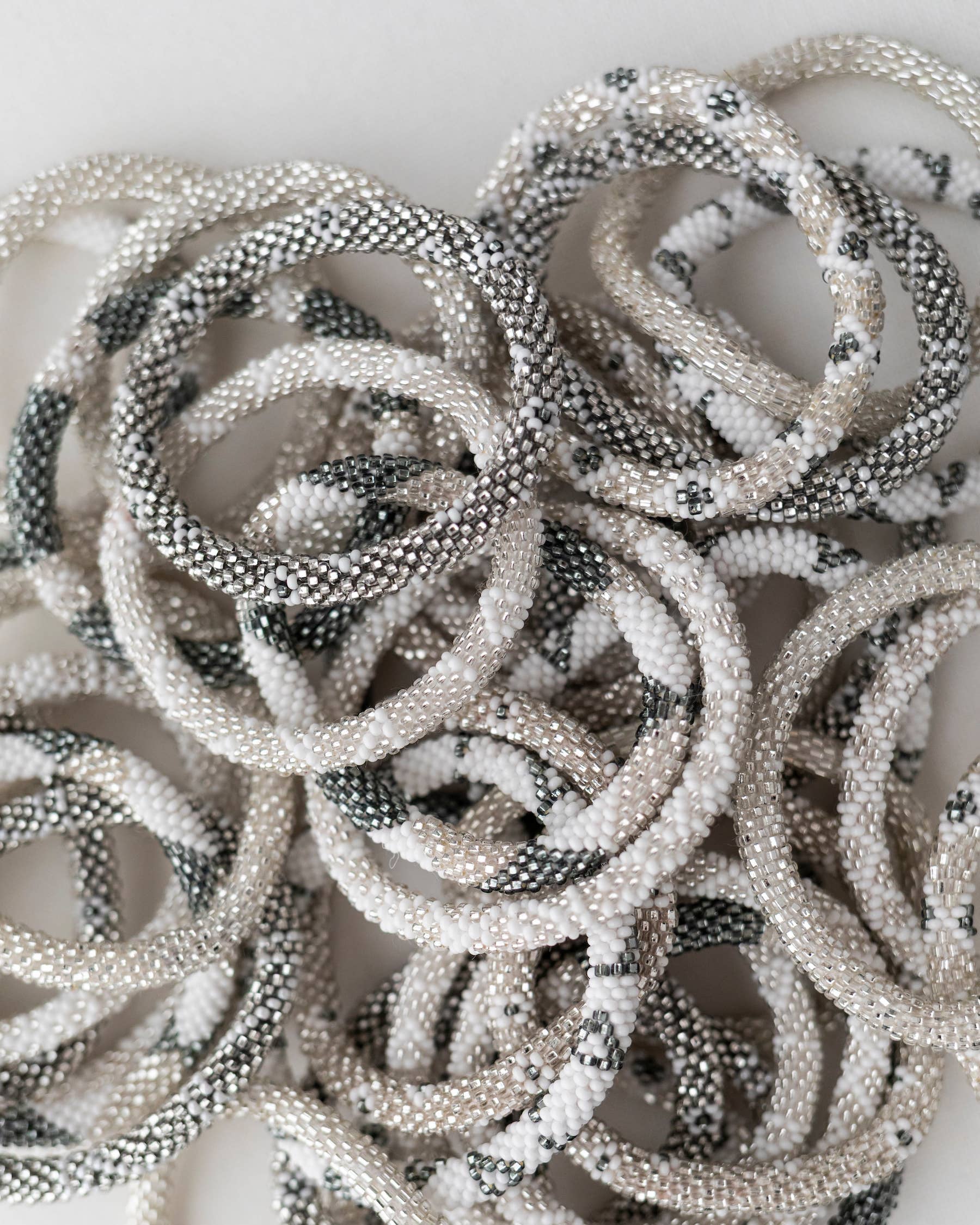 A pile of beaded elastic hair ties in a textured pattern of white, black, and gray beads on a plain white background.