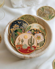 Set of decorative coasters with desert-themed designs in a ceramic dish on a white surface.