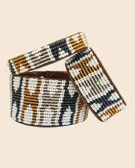 Three beaded bracelets with a geometric pattern of white, black, brown, and gold beads, displayed on a light blue background.