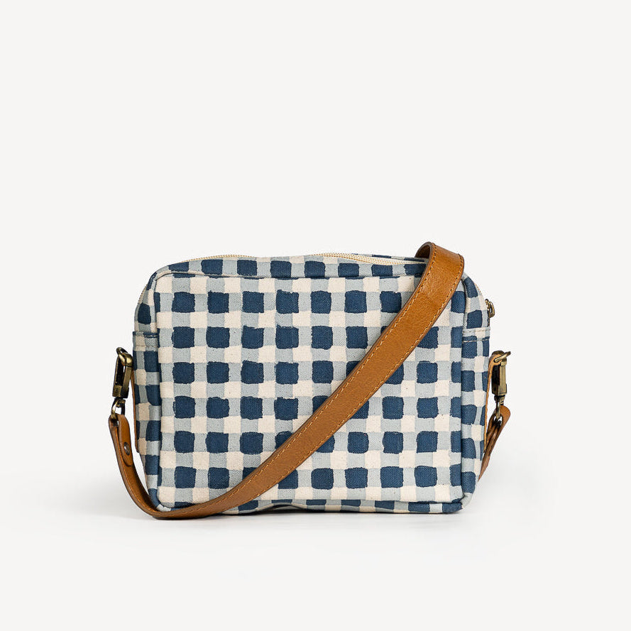 Crossbody bag with blue and white checkered pattern and brown strap on a light gray background