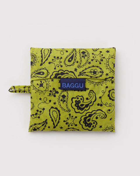A square fabric pouch with a black paisley pattern on a yellow-green background, featuring a small blue brand label that reads BAGGU and a matching fabric loop on the left side, photographed on a light gray background.