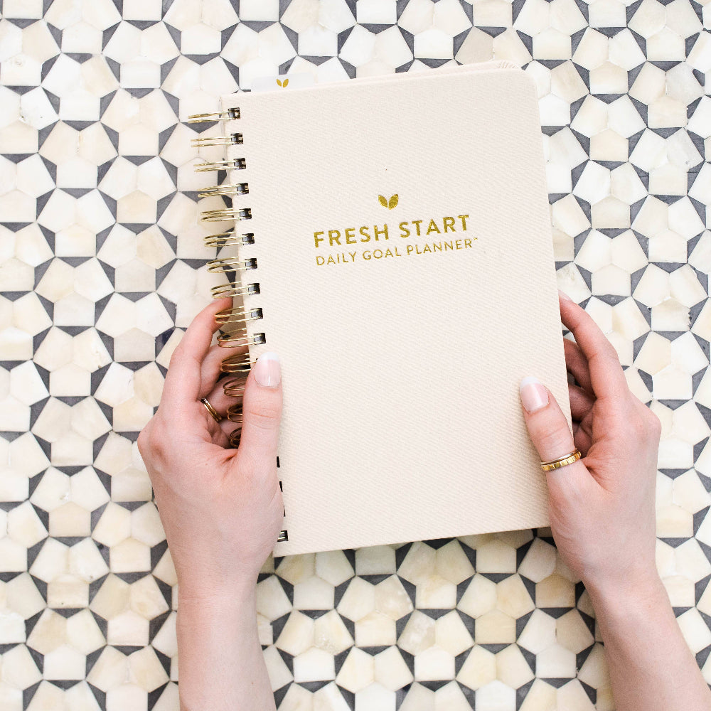Hands holding a 'Fresh Start Daily Goal Planner' on a geometric patterned surface