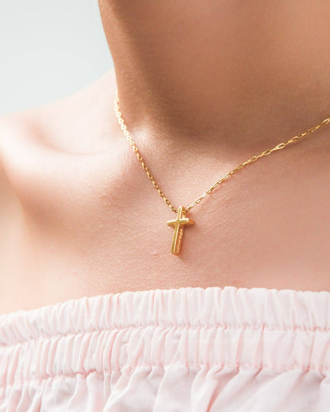 Gold necklace with a cross pendant on a person wearing a white top.