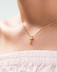 Gold necklace with a cross pendant on a person wearing a white top.