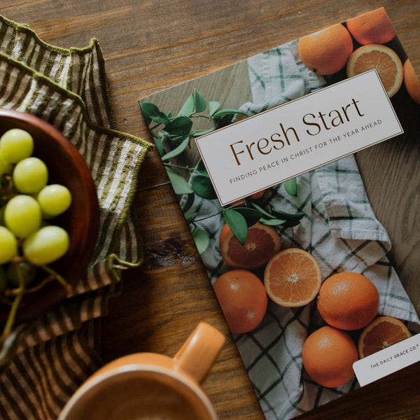 Book titled 'Fresh Start' with oranges on a wooden surface next to grapes and a mug.