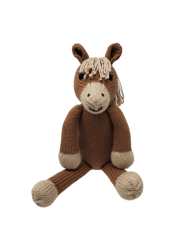 Knitted horse toy next to a pillow with a whale design on a striped blanket