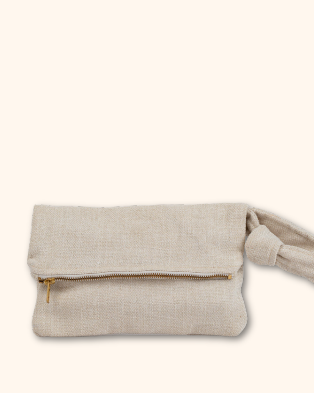 A light beige linen clutch bag with a gold zipper and a knotted strap detail, shown against a solid cream background.