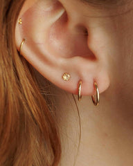 Close-up of a person's ear showcasing multiple gold piercings, including two small hoop earrings, a larger hoop, a floral stud, and a cartilage hoop.