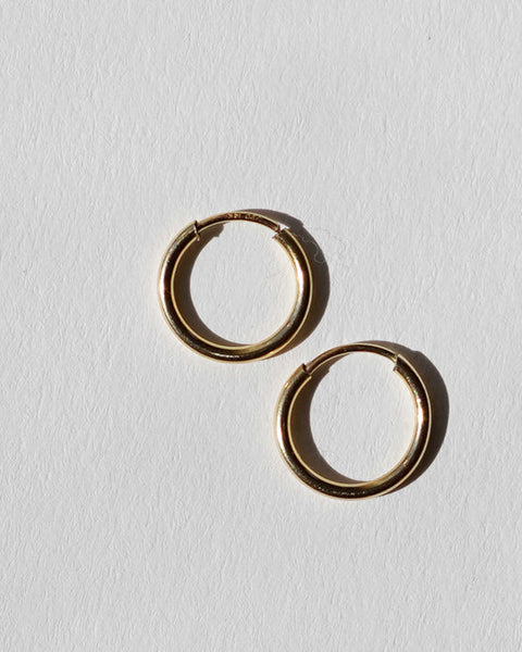 A pair of gold hoop earrings on a textured white background.