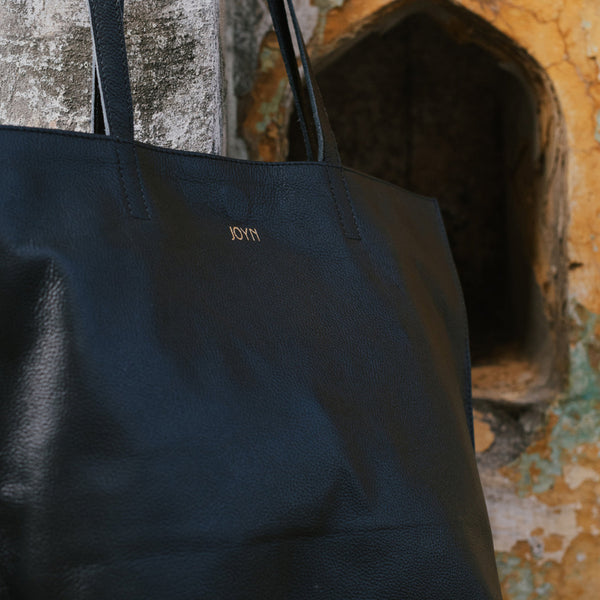 Black tote bag with 'JOYN' branding against a textured wall background