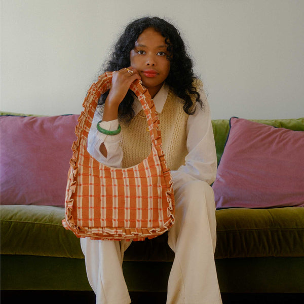 Woman holding an orange plaid bag on a green couch with pink cushions
