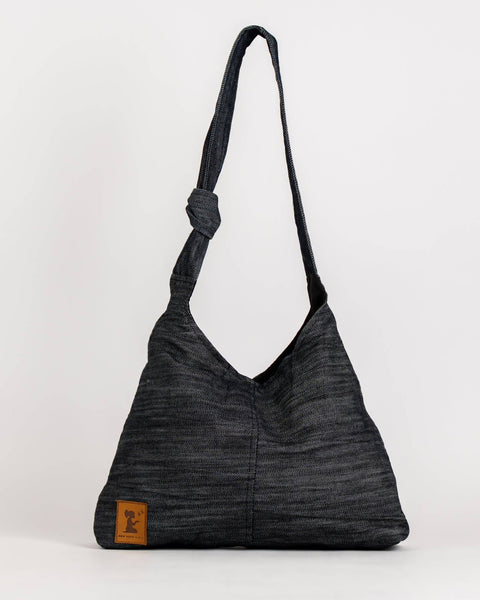 A dark gray textured slouchy shoulder bag with a single strap and a small brown leather brand patch on the bottom left, set against a plain white studio background.