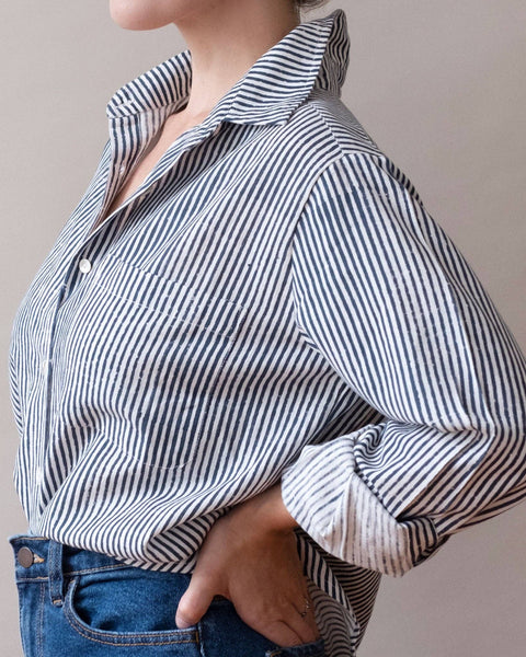 Person wearing a navy and white striped shirt with rolled-up sleeves against a plain background