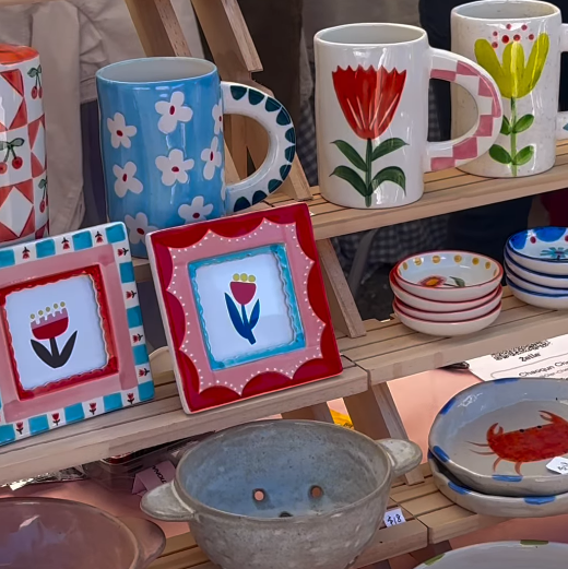 Display of colorful ceramic mugs and bowls with floral and abstract designs.