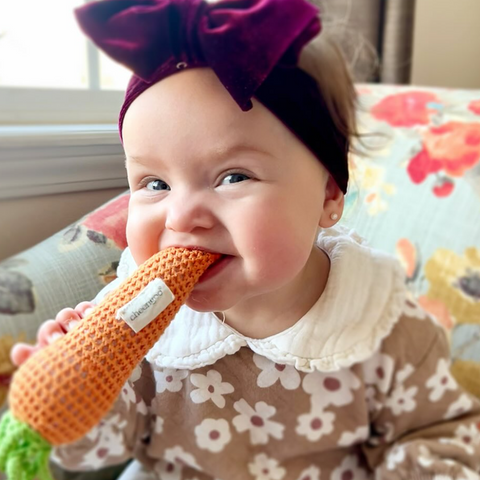 Baby with a purple bow and a carrot-shaped toy