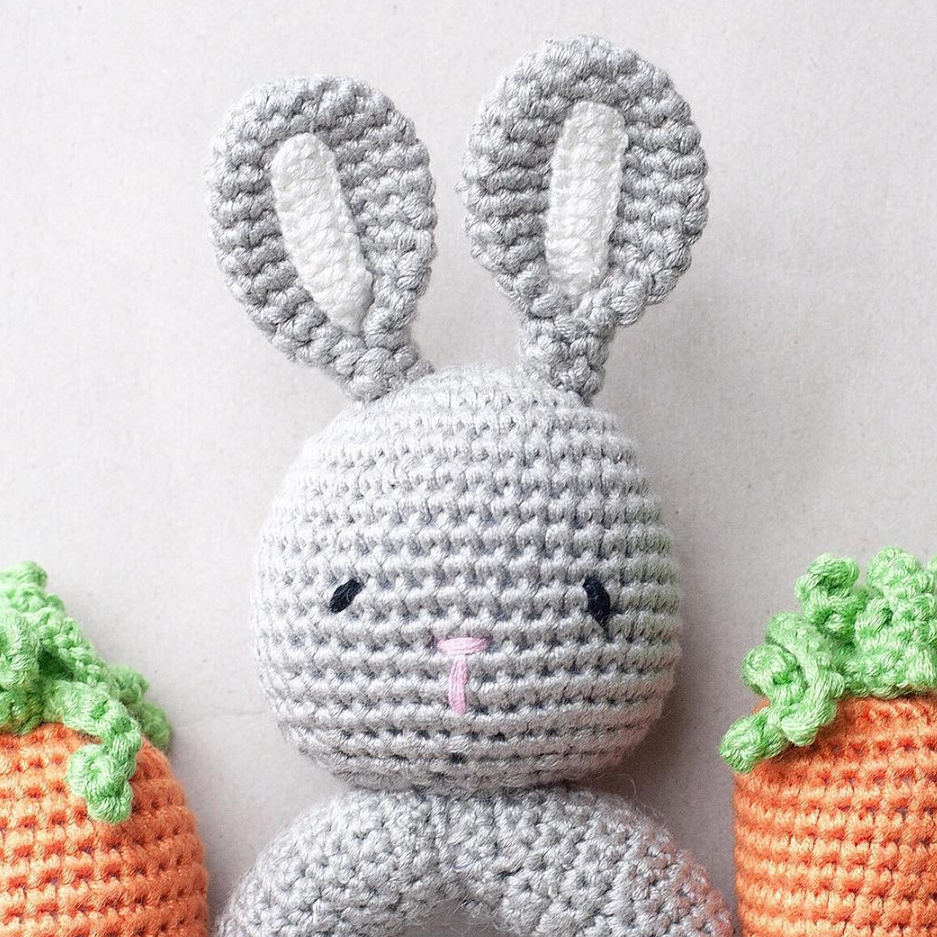 Crocheted gray bunny with carrot toys on a light background
